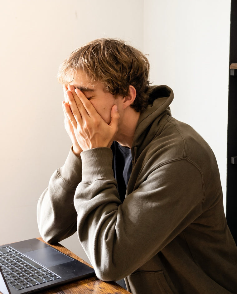 Un homme assis à son bureau, les mains sur le visage, devant son ordinateur